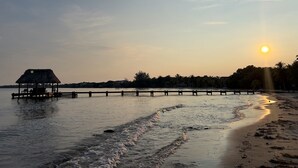 A beach with a thatched-roof hut and wooden pier extending into calm waters.
