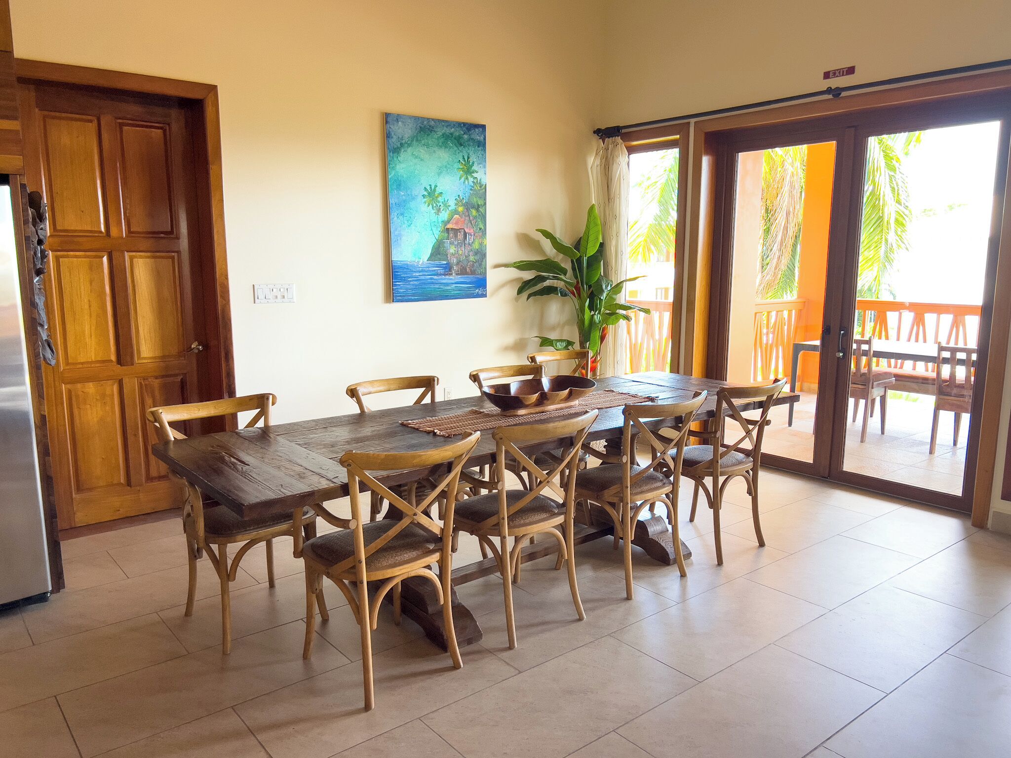 Un'area pranzo con tavolo e sedie in legno, un quadro appeso al muro e una porta scorrevole in vetro che dà su un patio esterno.