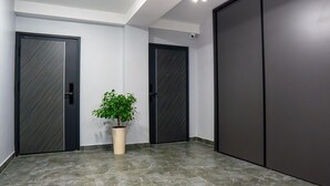 A hallway with two dark-colored doors, a potted plant, and tiled flooring. - SingKolSuites (Bishkek)