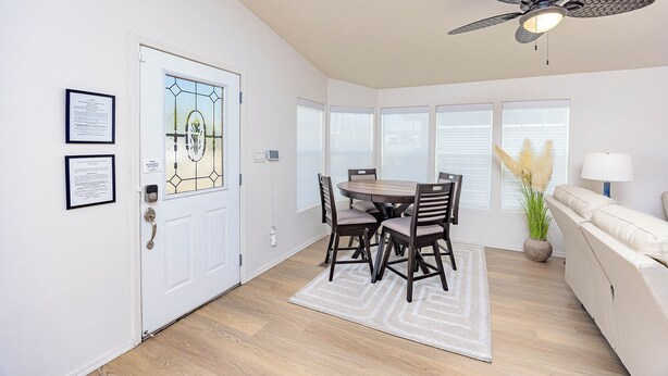 A dining area with a table and chairs, a ceiling fan, a sofa, and a window with blinds.
