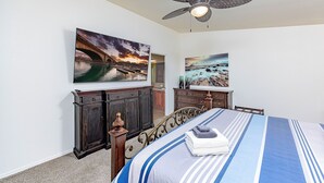 A bedroom with a bed, a ceiling fan, two paintings, a dresser, and a cabinet.