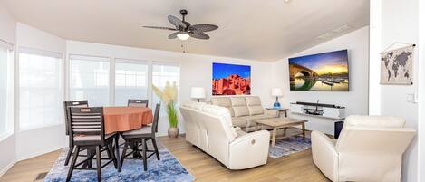 A modern living room with a dining area, white furniture, and large windows.