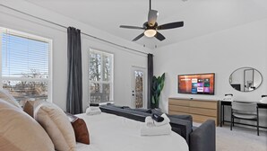 Een moderne hotelkamer met een groot bed, een bureau, een stoel, een televisiescherm waarop streamingdiensten worden getoond en een plafondventilator.