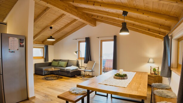 A modern kitchen with wooden beams, a refrigerator, a dining table, and a sofa. - 90-square-meter vacation rental for 2 to 6 people (Staudach-Egerndach)