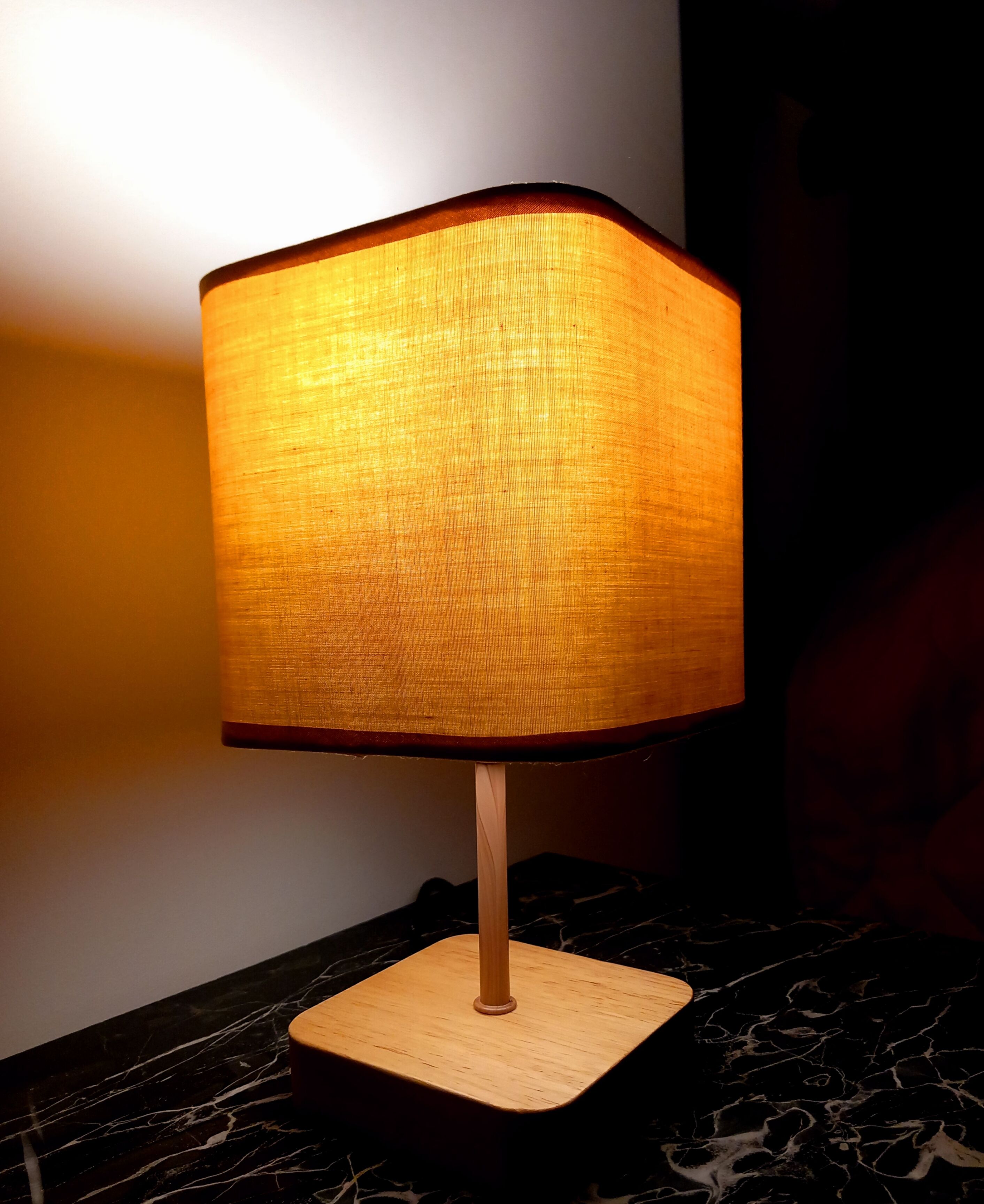 Une lampe de table avec un pied carré et un abat-jour en tissu, posée sur une surface en marbre.