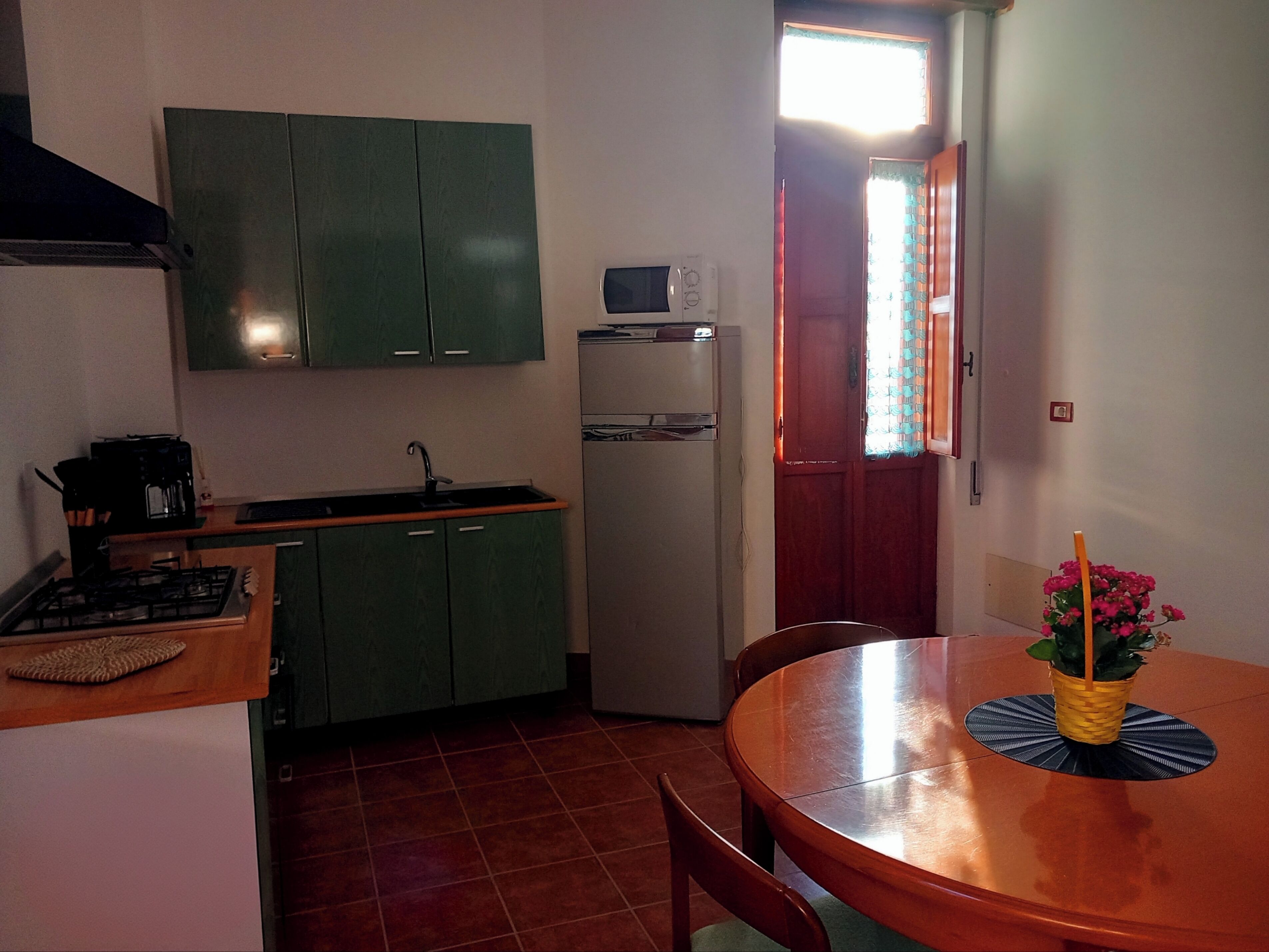 Una cocina compacta con armarios verdes, un refrigerador blanco, una estufa y una mesa de comedor con una silla.