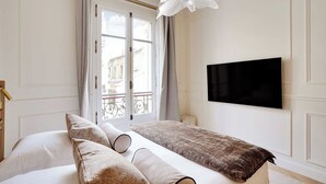 A hotel room with a bed, a TV mounted on the wall, and a window with curtains. - Elegant A/C Apt 2BR/6P – Paris 17th/Monceau (Paris)