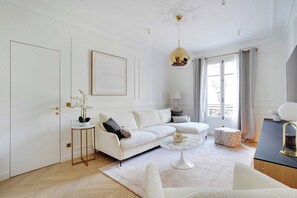 Una sala de estar moderna con un sofá blanco, una mesa de centro redonda e iluminación colgante.