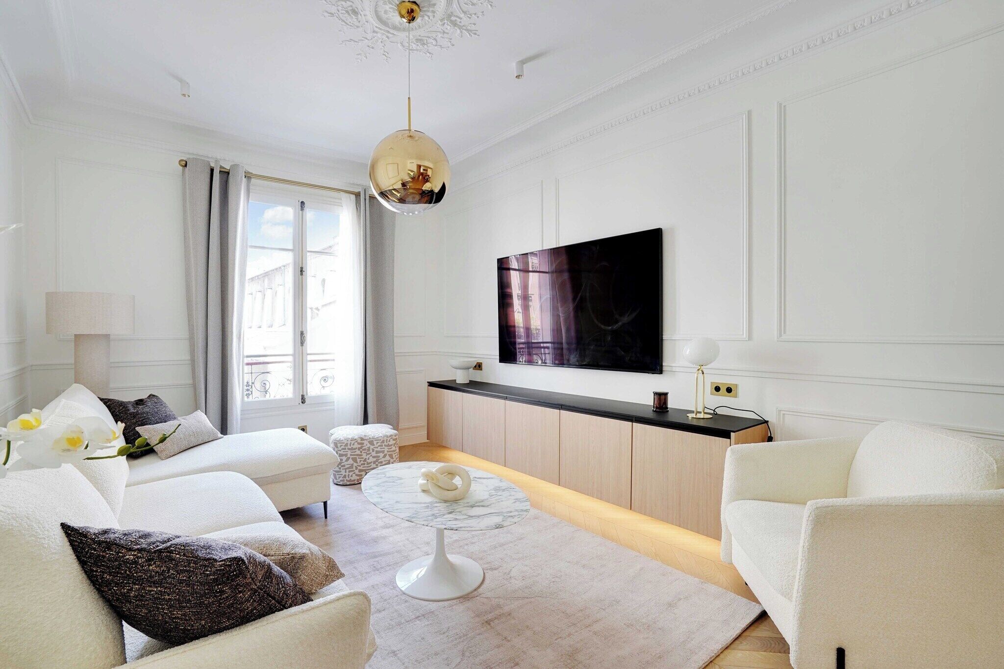 Een moderne woonkamer met een bank, een rond salontafeltje en een flatscreen televisie aan de muur.