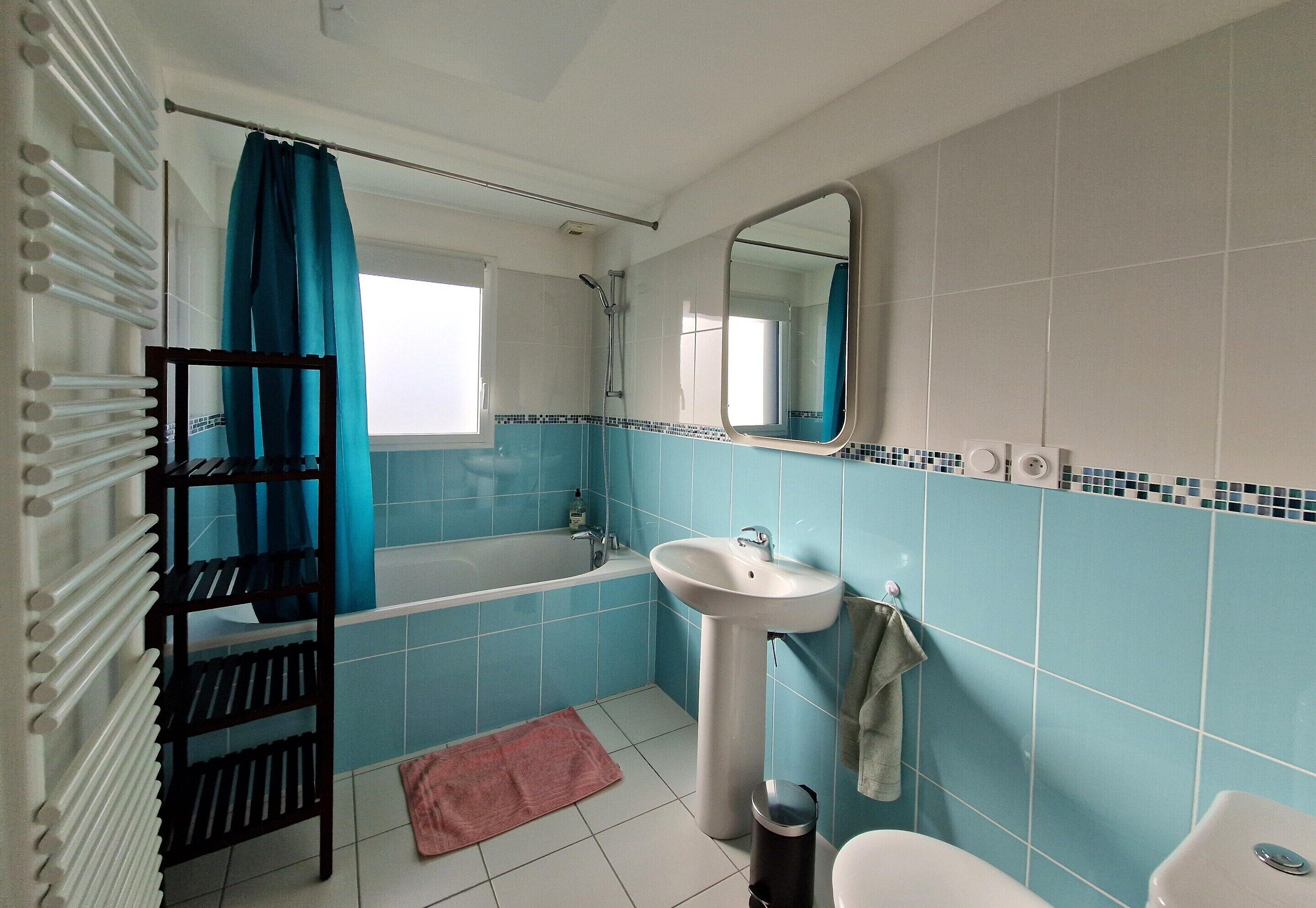 Ein Badezimmer mit Badewanne, Waschbecken und Toilette. Ein Handtuchhalter und ein Mülleimer sind ebenfalls vorhanden.