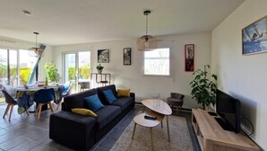 Una sala de estar moderna con sofá, mesa de centro y mueble para la televisión. Hay un comedor con mesa y sillas.