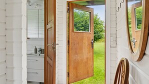 Eine Holztür führt zu einem grünen Hof, ein Spiegel an der Wand und ein Badezimmer mit Waschbecken und Handtuchhalter.