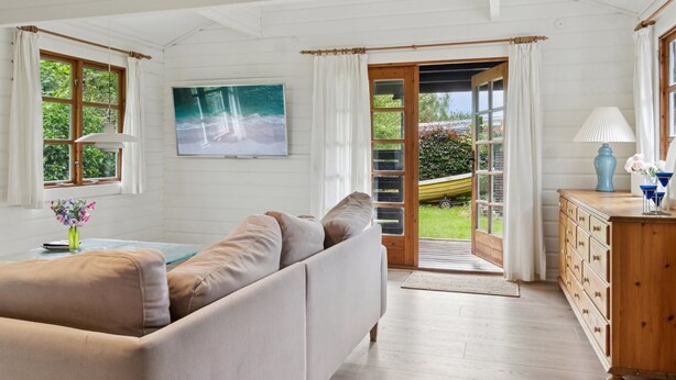 Ein gemütliches Zimmer mit einer Couch, einem hölzernen Schminktisch und einem großen Fenster mit Blick auf Grünflächen und ein Boot.