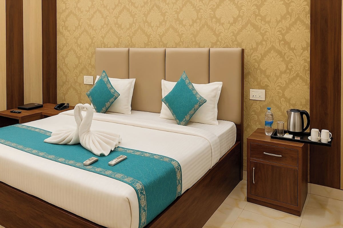 Quarto de hotel com uma cama grande, duas almofadas, mesa de cabeceira com telefone, garrafa de água, chaleira e uma xícara em um tabuleiro.