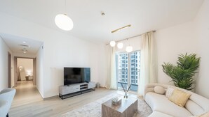 Ein modernes Wohnzimmer mit Flachbildfernseher, einer Couch, einem Couchtisch und einem großen Fenster mit Vorhängen.