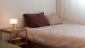 A neatly made bed with a light-colored duvet, a brown pillow, and a bedside table with a lamp and a basket.