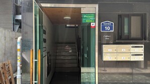 A building entrance with a glass door, a staircase leading inside, a sign with a phone number, and a mailbox.