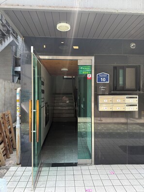 A building entrance with a glass door, a staircase leading inside, a sign with a phone number, and a mailbox.