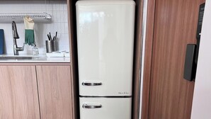 A white refrigerator with a handle and a freezer compartment, placed in a kitchen with wooden cabinets and a white countertop.