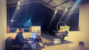 A man seated at a desk with a laptop, a small potted plant, and a decorative item on the counter. - Pench Kulamama Safari Resort (Kurai)