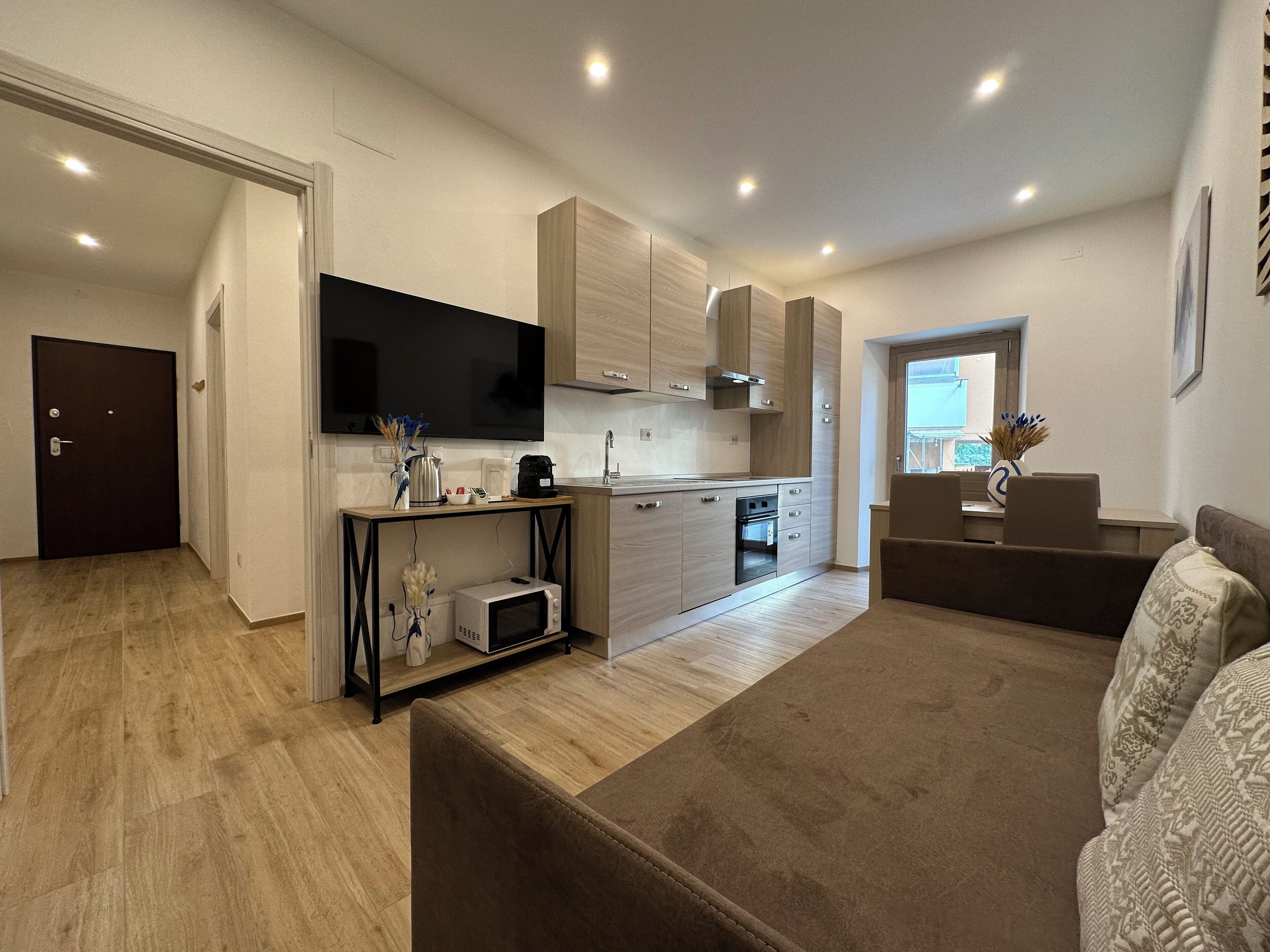 A modern kitchen with wooden cabinets, a built-in oven, and a flat-screen TV.