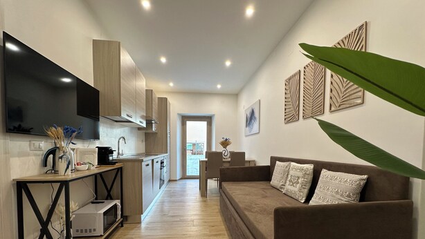 A modern living room with a sofa, TV, kitchen area, and decorative wall art. - NG Collection il Barbagia (Alghero)
