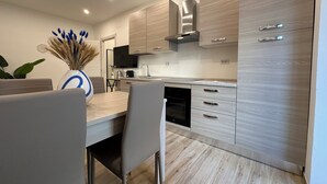 A modern kitchen with light wood cabinetry, a built-in oven, and a dining area with a table and chairs. - NG Collection il Barbagia (Alghero)