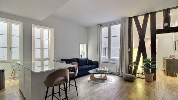 Un salon moderne avec un coin cuisine, comprenant un canapé bleu, une table basse ronde et un coin repas avec des tabourets de bar.