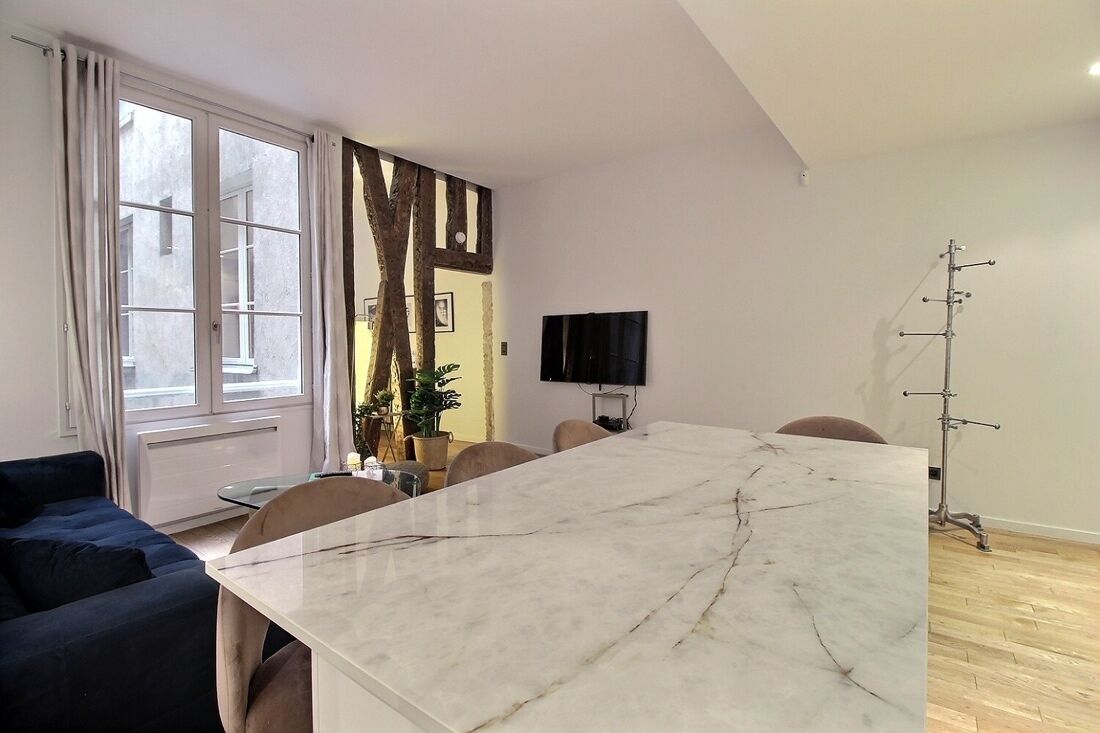 A modern living room with a large marble table, a blue sofa, and a television on the wall.