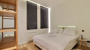 Une chambre moderne avec un grand lit, des étagères intégrées et une fenêtre équipée de rideaux occultants.