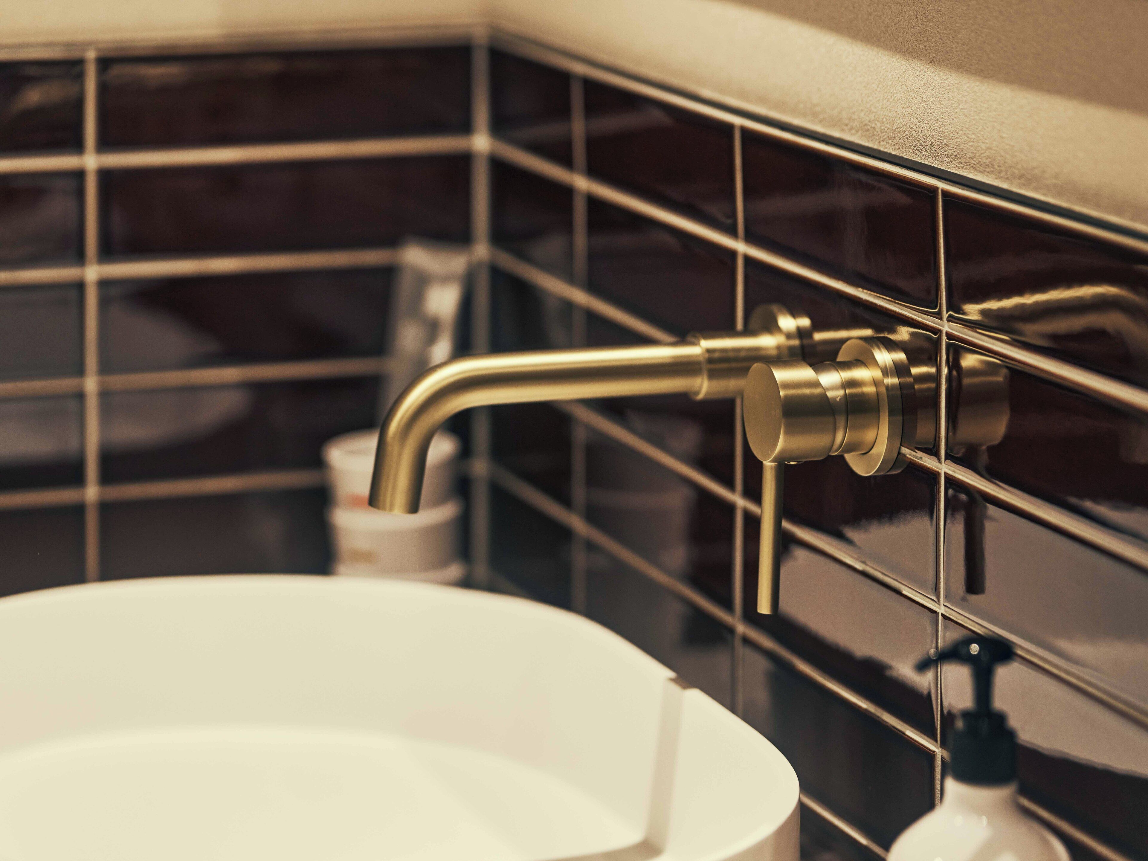 A bathroom with a white sink, a gold faucet, and a soap dispenser.