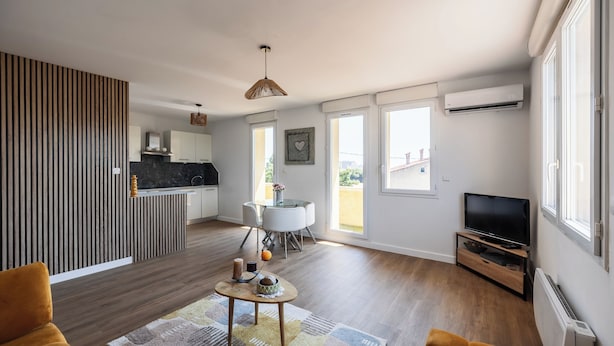 A modern living room with a sofa, a coffee table, and a TV. There is a kitchen area with a dining table and chairs. - Apartment close to the beach with a view! (Port-de-Bouc)