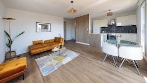 A modern living room with a sofa, coffee table, and a dining area with chairs. - Apartment close to the beach with a view! (Port-de-Bouc)