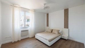 A bedroom with a bed, a ceiling fan, a window with curtains, and a radiator. - Apartment close to the beach with a view! (Port-de-Bouc)