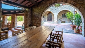 An outdoor patio with a wooden table and benches, stone arches, and potted plants.