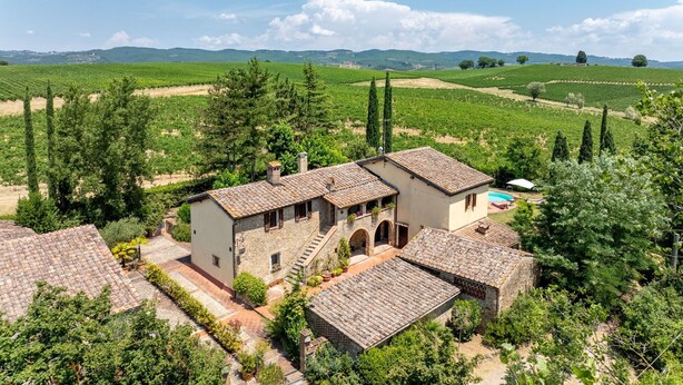 A villa with a courtyard, surrounded by vineyards and hills.