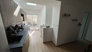 A modern kitchen with a central island, a dining area with a table and chairs, and a view of the outside through a sliding glass door.