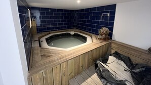 A bathroom with a wooden bathtub, blue tiles, and a wooden bench.