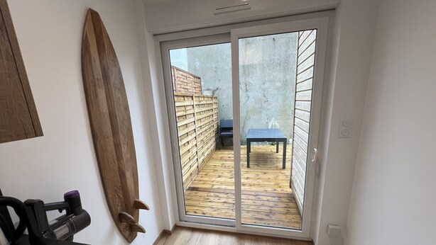 A room with a sliding glass door leading to an outdoor area with a wooden deck and a table.