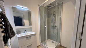 Um banheiro moderno com chuveiro envidraçado, pia branca com espelho acima e porta-toalhas com toalha.
