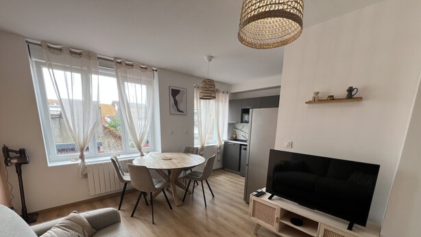 Uma sala de estar moderna com um sofá, uma mesa de jantar com cadeiras, uma área de cozinha e uma televisão em um móvel.