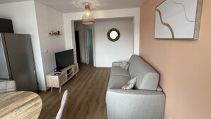 Uma sala de estar moderna com um sofá cinzento, uma mesa de jantar de madeira e uma televisão sobre um móvel de madeira.