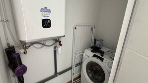 A compact laundry room with a washing machine, a water heater, and a vacuum cleaner.
