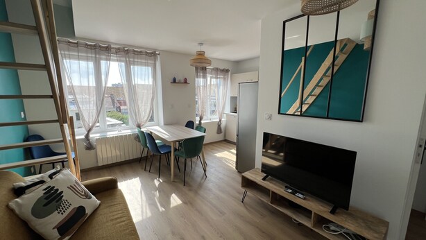 A modern living room with a sofa, a TV, a dining table with chairs, a ladder, and a large window with curtains.