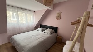 A bedroom with a bed, a wooden ladder, a hanging macrame wall decoration, and a window with sheer curtains.