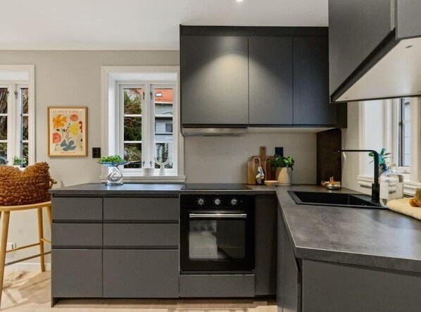 Una cocina moderna con armarios oscuros, horno integrado y una isla grande con un lavamanos.