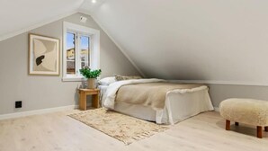 A bedroom with a sloped ceiling, a bed, a small table with a plant, a rug, and a bench.