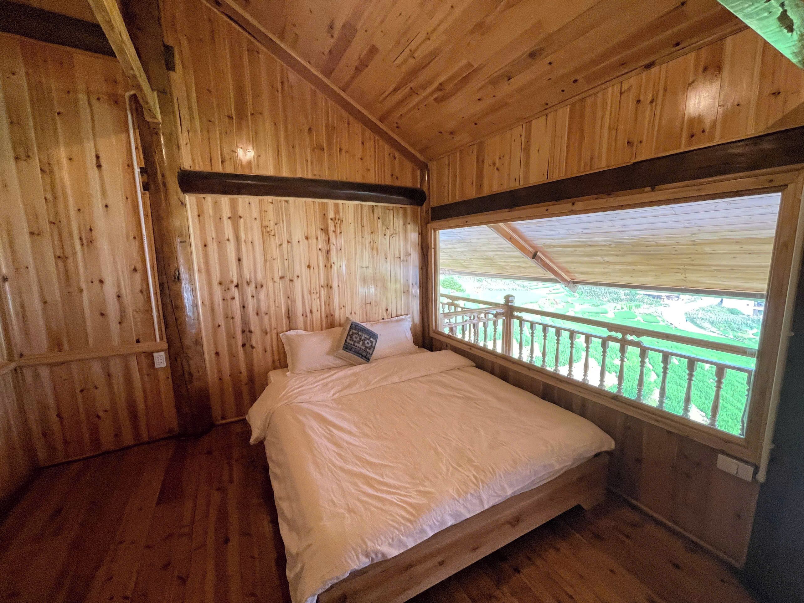 Camera da letto in una baita di legno, con un letto, una finestra vista su un paesaggio verde e un soffitto in legno.