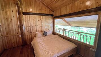 Camera da letto in una baita di legno, con un letto, una finestra vista su un paesaggio verde e un soffitto in legno.