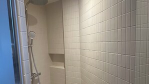 Un baño moderno con paredes de azulejos blancos, zona de ducha y desagüe visible.